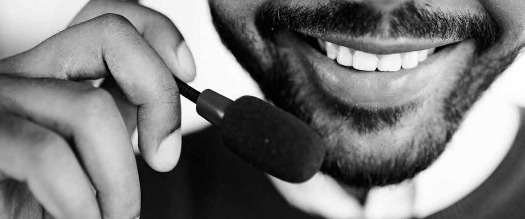 Alt text for web: Bearded man smiling while wearing a headset with a microphone near his mouth.