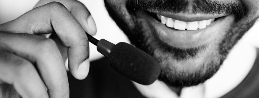 Alt text for web: Bearded man smiling while wearing a headset with a microphone near his mouth.