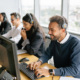 Customer service team members wearing headsets while working at computer desks in a bright office.