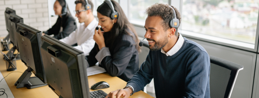 Customer service team members wearing headsets while working at computer desks in a bright office.